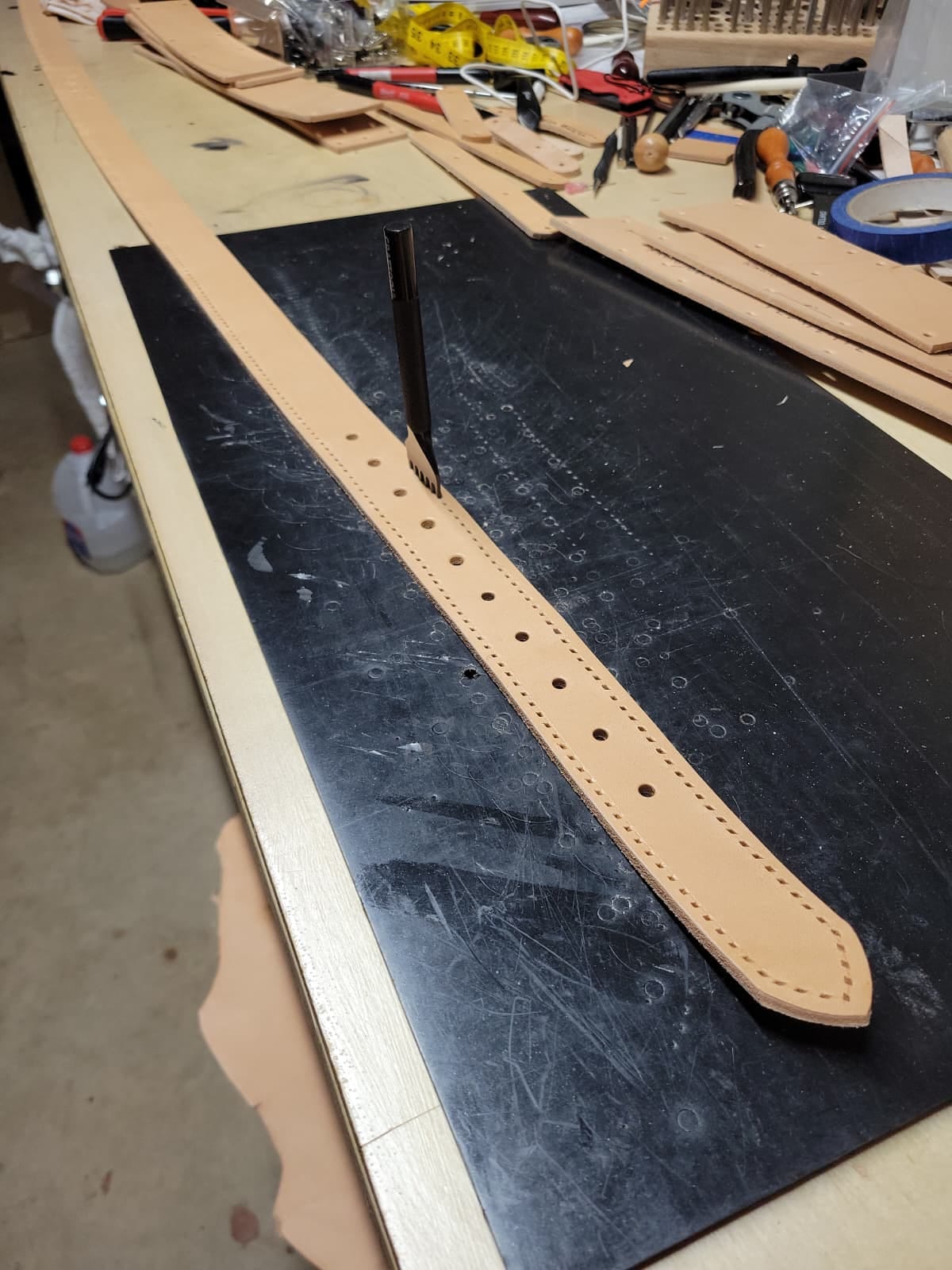 A cut leather blank on the bench with its holes punched to length